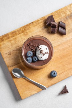 Krem şantili çikolatalı puding ve ahşap bir tahtada taze yaban mersini kaşık ve çikolata parçalarıyla arka planda. Ev yapımı kremalı tatlı ya da panna cotta konsepti. Üst görünüm.