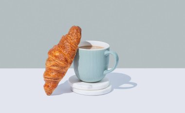 Taze kruvasan ve kapuçino ya da mermer üzerine kahve gölgeli beyaz ve yeşil bir arka planda duruyor. Cafe reklamları ya da Fransız kahvaltı konsepti için modaya uygun yaratıcı bir tasarım. Ön görünüm ve boşluk kopyala.