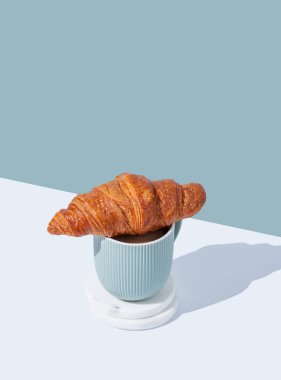 Bir fincan kapuçino üzerine taze kruvasan ya da beyaz ve mavi arka planda gölgeli latte kahve. Cafe reklamları ya da Fransız kahvaltı konsepti için modaya uygun yaratıcı bir tasarım. Üst görünüm ve kopyalama alanı.