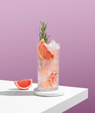 Mor arka planda, greyfurt, biberiye ve buzlu, gölgeli bir bardakta taze bir kokteyl. Yaz turunçgil içeceği ya da kafe reklamları için limonata konsepti. Boşluğu kopyala.