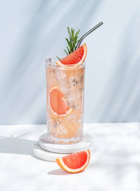 Greyfurt, biberiye ve buzlu beyaz mavi arka planda gölgeli bir bardakta taze bir kokteyl. Yaz turunçgil içeceği ya da kafe reklamları için limonata konsepti. Ön görünüm ve boşluk kopyala.