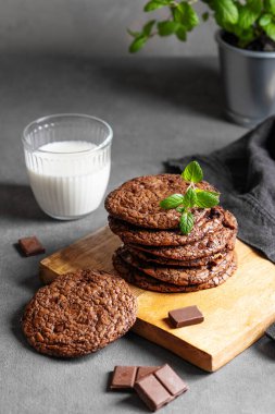 Bir bardak süt ve peçeteyle birlikte siyah arka planda tahta bir tahtada bir yığın çikolatalı kurabiye. Lezzetli ev yapımı pişirme kavramı. Boşluğu kopyala.