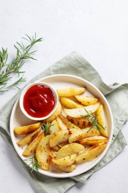 Baharatlı fırınlanmış patates kamaları, taze biberiye ve hafif bir arka planda taze bitki ve peçeteyle birlikte domates sosu. Ev yapımı vejetaryen atıştırmalık konsepti. Üst görünüm ve kopyalama alanı