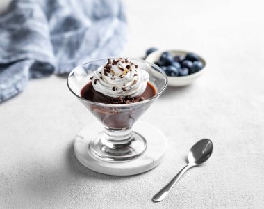 Hafif arka planda krem şantili çikolatalı puding, böğürtlen, kaşık ve peçeteli. Ev yapımı kremalı tatlı ya da panna cotta konsepti. Boşluğu kopyala.