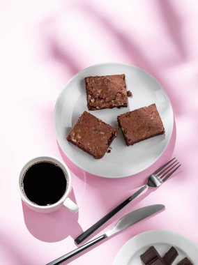 Bir tabak fındıklı çikolatalı kek ve bir fincan espresso kahvesi. Pembe arka planda, çatal ve gölgeli. Kahvaltı için ev yapımı tatlı hamur işi kavramı. Üst görünüm ve kopyalama alanı.