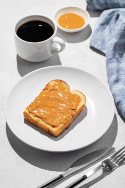 Hafif arka planda bir tabakta fıstık ezmeli tost bir fincan taze kahve ve peçeteyle birlikte. Kahvaltıda tatlı beslenme ve sağlıklı atıştırmalıklar kavramı. 