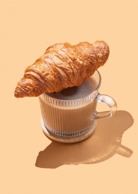 Bir fincan kapuçino üzerine taze kruvasan ya da gölgeli turuncu bir arka planda latte. Cafe reklamları ya da Fransız kahvaltı konsepti için modaya uygun yaratıcı bir tasarım. Üst görünüm ve kopyalama alanı.