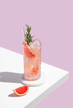 Mokktail 'i greyfurtla, biberiyeyle ve gölgeli pembe bir arka planda buzla tazeliyorum. Yaz turunçgil içeceği ya da kafe reklamları için limonata konsepti. Üst görünüm ve kopyalama alanı.