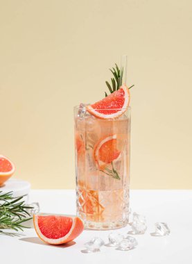 Greyfurt, biberiye ve buzlu beyaz sarı arka planda gölgeli bir bardakta taze bir kokteyl. Yaz turunçgil içeceği ya da kafe reklamları için limonata konsepti. Ön görünüm.