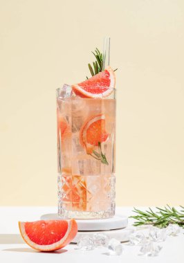 Beyaz sarı arka planda gölgeli bir bardakta greyfurt, biberiye ve buzla mocktail tazeleyici. Yaz turunçgil içeceği ya da kafe reklamları için limonata konsepti. Ön görünüm