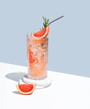 Üzüm suyu, biberiye ve buzlu mocktail 'i beyaz mavi arka planda gölgeli bir bardakla tazeliyorum. Yaz turunçgil içeceği ya da kafe reklamları için limonata konsepti. Boşluğu kopyala.