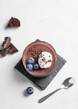 Krem şantili çikolatalı puding ve siyah kaplamalı taze yaban mersini kaşık ve çikolata parçalarıyla birlikte. Ev yapımı kremalı tatlı ya da panna cotta konsepti. Üst görünüm