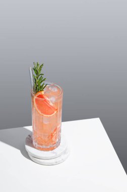 Gri arka planda, greyfurt, biberiye ve buzlu, gölgeli bir bardakta taze bir kokteyl. Yaz turunçgil içeceği ya da kafe reklamları için limonata konsepti. Üst görünüm ve kopyalama alanı.