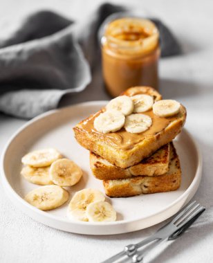 Fıstık ezmeli tost. Arka planda hafif bir tabakta muzlu. Kavanoz ve peçeteyle yakın plan. Amerikan kahvaltısı için tatlı beslenme ve sağlıklı atıştırmalıklar kavramı. 