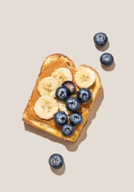 Bej izole edilmiş gölgeli arka planda muz ve yabanmersinli fıstık ezmeli tost. Reklam menüsü veya afiş için Amerikan kahvaltısı için tatlı ve sağlıklı atıştırmalıklar kavramı. Üst görünüm