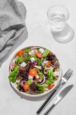 Kiraz domatesli sebze salatası (Yunan salatası), beyaz peynir, marul, zeytin ve kırmızı soğanlı bir tabakta bir bardak suyla birlikte. Sağlıklı beslenme konsepti. Üst görünüm.