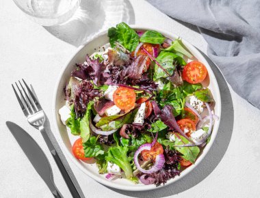 Kiraz domatesli sebze salatası (Yunan salatası), beyaz peynir, marul, zeytin ve kırmızı soğanlı cam bardak su ve gölgede bir tabakta. Sağlıklı beslenme kavramı. 