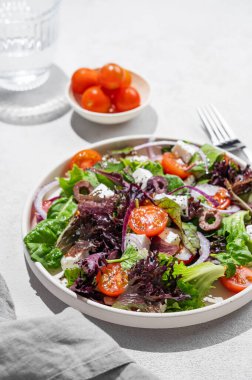 Kiraz domatesli sebze salatası (Yunan salatası), beyaz peynir, marul, zeytin ve kırmızı soğanlı bir tabakta bir bardak suyla birlikte. Sağlıklı beslenme konsepti. Boşluğu kopyala.