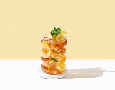 Limonlu buzlu buzlu buzlu çay ve gölgeli beyaz ve sarı arka planda bir bardak nane. Ferahlatıcı içecek ya da limonata, menü reklam modeli. Ön görünüm ve boşluk kopyala.