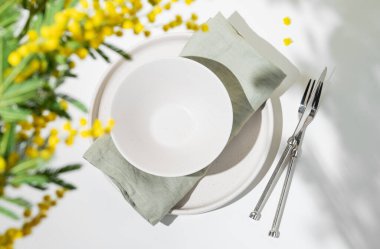 Kadınlar günü, düğün ya da anneler günü için açık arkaplanda sarı mimoza çiçekleri olan bahar kutlaması için sofra kurulumu. Restoran menüsü konsepti. Üst görünüm ve kopyalama alanı.