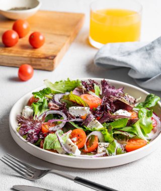 Hafif arka planda bir tabakta domates, peynir, marul, zeytin ve soğanlı sebze salatası (Yunan salatası) ve bir bardak meyve suyu. Sağlıklı beslenme kavramı. 