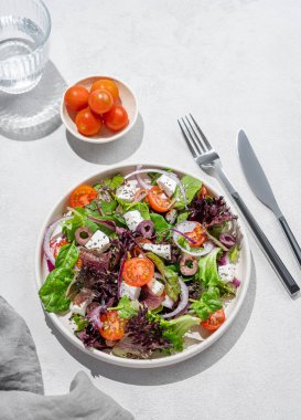 Kiraz domatesli sebze salatası (Yunan salatası), beyaz peynir, marul, zeytin ve kırmızı soğanlı bir tabakta bir bardak suyla birlikte. Sağlıklı beslenme konsepti. Üst görünüm.