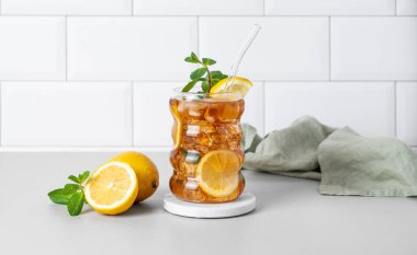 Limon, buz ve naneli buzlu çay. Mutfak tezgahında narenciye meyveleri ve beyaz tuğlalı duvar arkası olan bir bardak. Ferahlatıcı içecek ya da limonata modası. Ön görünüm ve boşluk kopyala.