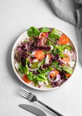Hafif arkaplanda kiraz domatesli sebze salatası (Yunan salatası), feta peyniri, marul, zeytin ve kırmızı soğan. Sağlıklı beslenme konsepti. Üst görünüm ve kopyalama alanı.