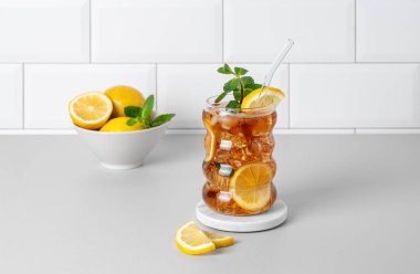 Limon, buz ve naneli buzlu çay. Mutfak tezgahında narenciye meyveleri ve beyaz tuğlalı duvar arkası olan bir bardak. Ferahlatıcı içecek ya da limonata modası. Ön görünüm ve boşluk kopyala.