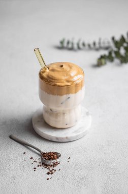 Kore kremalı Dalgona kahvesi, açık bir arka planda kaşık ve sabah gölgesi ile. Hazır kahve, şeker, süt ve buzla birlikte iç. Moda tatlı tatlı konsepti. 