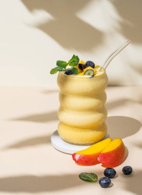 Bej arka planda bir bardakta mango, muz ve yaban mersinli meyve suyu ve gölgeyle birlikte. Sağlıklı beslenme ve detoks diyeti kavramı. Ön görünüm ve boşluk kopyala.