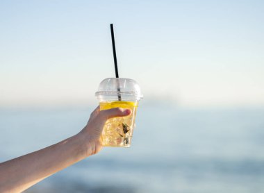 Denize karşı bir bardak limonata tutarken. Menü ya da pankart reklamı için ferahlatıcı bir içecek konsepti. Limon ve buzlu soğuk içecek. Metin için boş alan.