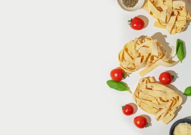Taze tagliatelle makarna yuvaları, kiraz domatesleri, fesleğen yaprakları, rendelenmiş peynir ve beyaz arka planda kurutulmuş otlar. İtalyan mutfağı konsepti. Üst görünüm ve kopyalama alanı.