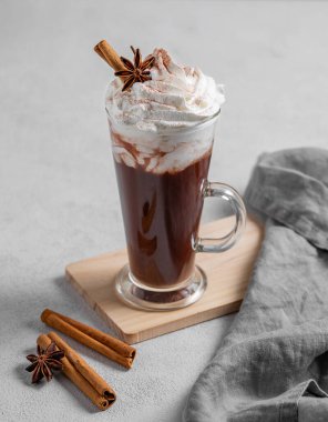 Krem şantili sıcak çikolata, tarçın ve hafif arka planda uzun bir bardakta baharatlar. Cafe reklamları veya afişler için tatlı içecek konsepti. Boşluğu kopyala.