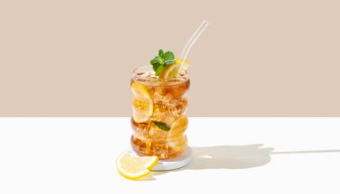 Limonlu buzlu buzlu buzlu çay ve bej renkli bir bardakta nane ve gölgeli beyaz arka plan. Ferahlatıcı içecek ya da limonata, menü reklam modeli. Ön görünüm ve boşluk kopyala.