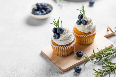 Krem peynirli kekler, taze yaban mersini ve biberiyeli ahşap tahta üzerinde taze böğürtlenli kekler. Lezzetli ev yapımı tatlı ya da tatil pişirme kavramı. Boşluğu kopyala