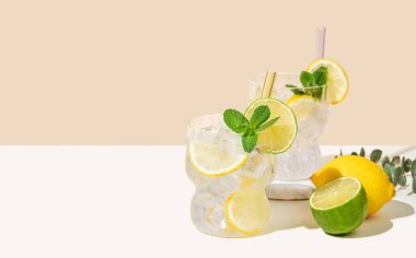 Limonlu, limonlu, naneli ve buzlu mojito. Beyaz bej arka planda meyveli limonata. Yaz modasına uygun soğuk içecek konsepti. Ön görünüm ve boşluk kopyala.
