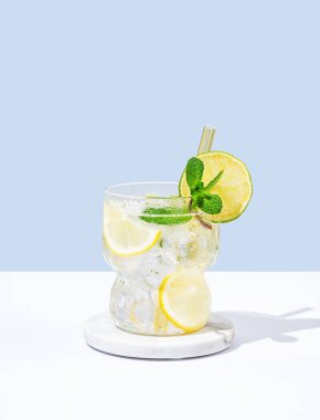 Limonlu mojito, naneli ve buzlu beyaz mavi arka planda gölgeli bir bardak. Yaz turunçgil içeceği ya da kafe reklamları için limonata konsepti. Ön görünüm ve boşluk kopyala.
