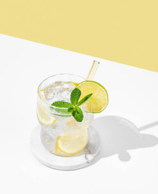 Limonlu, limonlu, naneli ve buzlu kokteyl. Beyaz sarı arka planda, gölgeli. Yaz turunçgil içeceği ya da kafe reklamları için limonata konsepti. Ön görünüm ve boşluk kopyala.