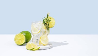 Limonlu, limonlu, biberiyeli ve buzlu kokteyl. Beyaz mavi arka planda, gölgeli ve meyveli. Yaz turunçgil içeceği ya da kafe reklamları için limonata konsepti. Ön görünüm