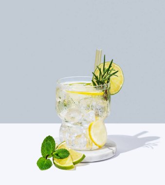 Limonlu, limonlu, biberiyeli mojito ve buzlu beyaz mavi arka planda gölgeli bir bardak. Yaz turunçgil içeceği ya da kafe reklamları için limonata konsepti. Ön görünüm, boşluğu kopyala