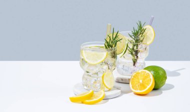 Limon, limon, biberiye ve buzlu iki bardak taze limonata. Beyaz mavi arka planda Citrus kokteyli mojito. Bar menüsü reklamları veya afişler için yaz modasına uygun içecek konsepti. Boşluğu kopyala.