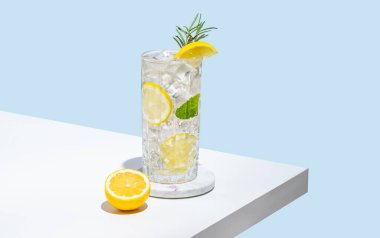 Limonlu limonata, biberiye ve buzlu bir bardak mavi arka planda beyaz bir masada. Yaz turunçgil içeceği ya da kafe reklamları için mojito kokteyli konsepti. Boşluğu kopyala.