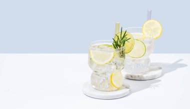 Limon, limon, biberiye ve buzlu iki bardak taze limonata. Beyaz mavi arka planda Citrus kokteyli mojito. Bar menüsü reklamları veya afişler için yaz modasına uygun içecek konsepti. Boşluğu kopyala.