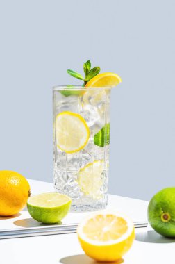 Limonlu, naneli ve buzlu beyaz mavi arka planda gölgeli ve meyveli bir bardakta iç. Yaz turunçgil limonatası ya da kafe menüsü reklam afişi için mojito kokteyli konsepti. Boşluğu kopyala.