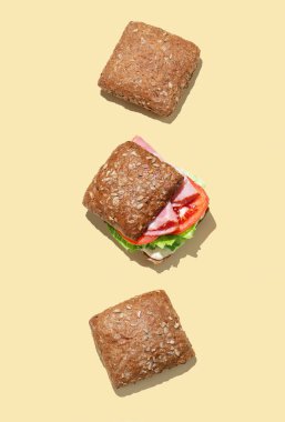 Jambonlu, marullu, domatesli ve sarı zemin üzerinde tam tahıllı ekmek soslu taze sandviç. Reklam afişi menüsü için sağlıklı beslenme kavramı. Üst görünüm, alanı kopyala.