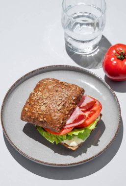 Prosciutto, domates, marul ve sostan yapılmış tahıllı sandviçle mavi zemin üzerinde bir bardak su. Kafe reklamları veya afişler için sağlıklı kahvaltı konsepti. Üst görünüm.