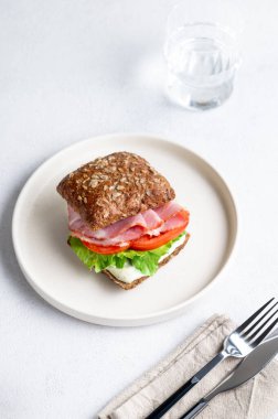 Jambonlu, peynirli, domatesli, marullu ve soslu tahıllı sandviç hafif bir zemin üzerinde bir bardak suyla. Sağlıklı ve diyet kahvaltı konsepti. Üst görünüm, alanı kopyala.
