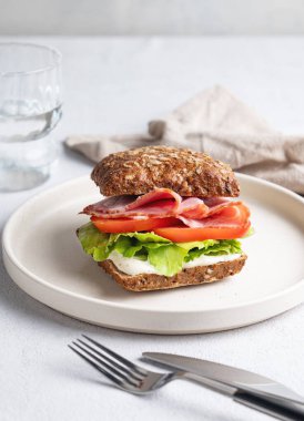 Jambonlu, peynirli, domatesli, marullu ve soslu tahıllı sandviç hafif bir zemin üzerinde bir bardak suyla. Sağlıklı ve diyet kahvaltı konsepti. Ön görünüm, boşluğu kopyala