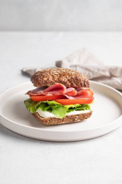 Jambonlu, peynirli, domatesli, salatalı ve soslu tahıllı sandviç, peçeteli bir tabakta. Sağlıklı ve diyet kahvaltı konsepti. Ön görünüm, boşluğu kopyala.